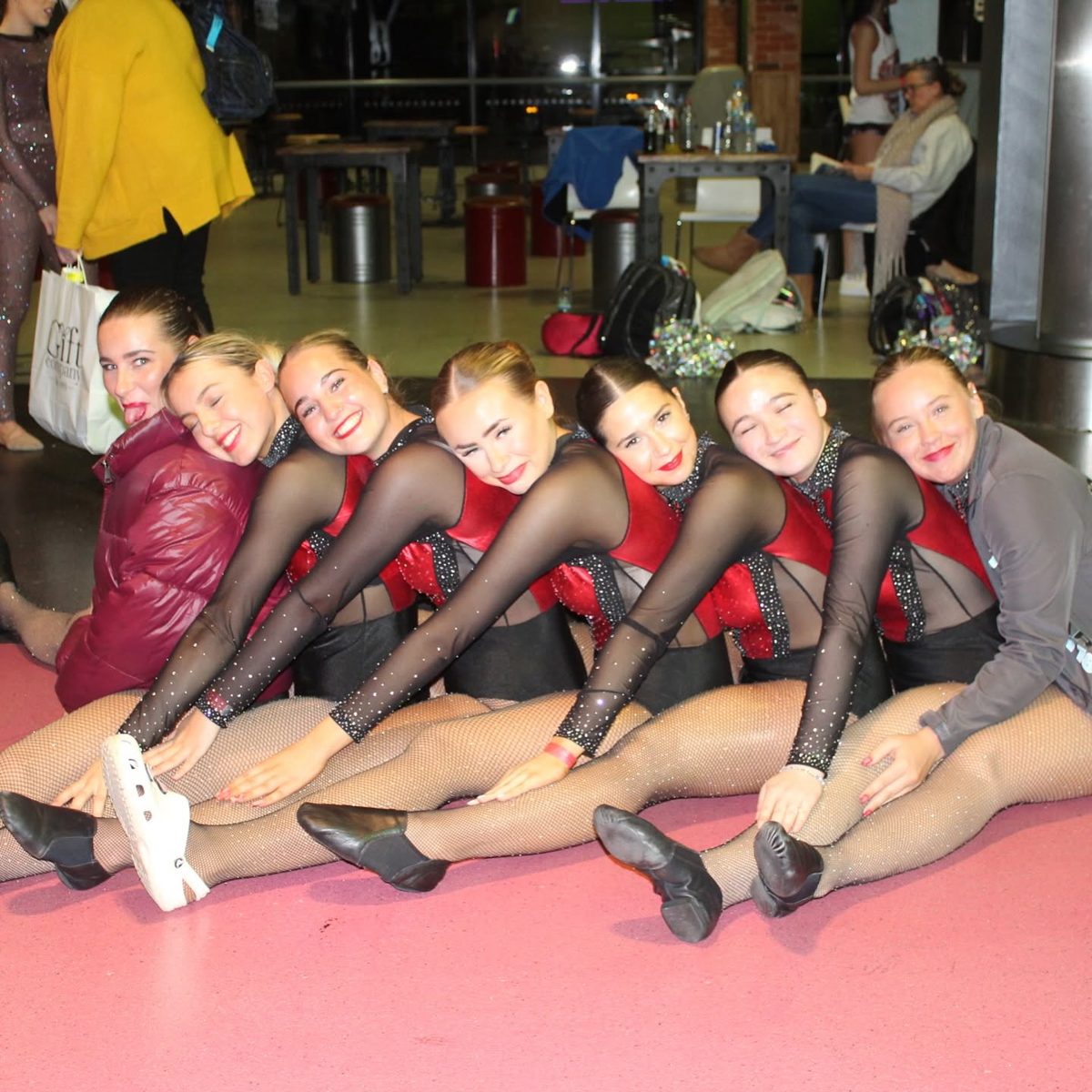 Tycoons senior dancers sitting in a line, laughing together backstage